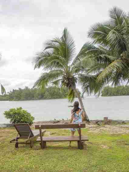 Rarotonga on a rainy day Girl standing in front of sun chair facing palm trees with strong wind and cloudy sky