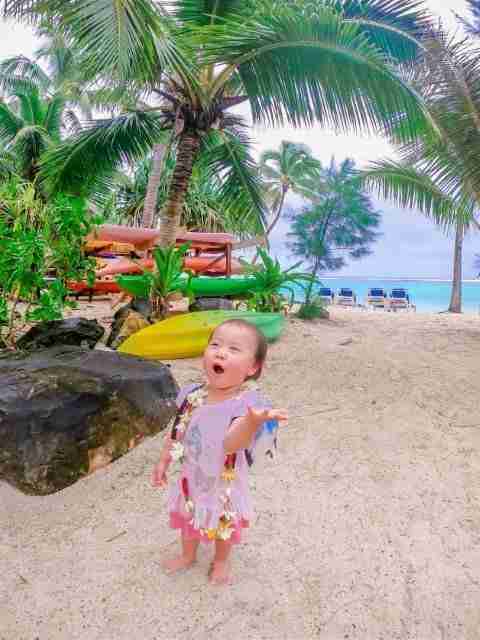 Toddler wearing flower necklace doing funny faces with kayaks at the resort for guests to borrow