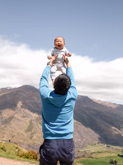 father holding baby up happy mountains