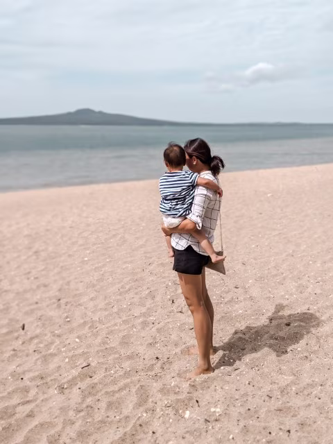 Mother holding baby in Mission Bay, Auckland Rangitoto volcano in background