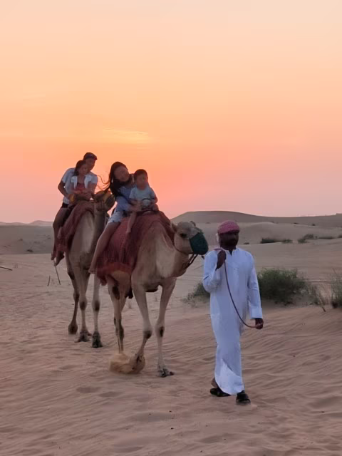 Millennial family travelling the world with kids, riding camel in Abu Dhabi desert safari, UAE Travel Adventure