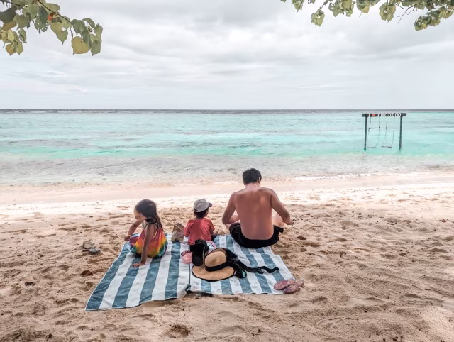 Family with two kids sitting beach towel on the sand in Thoddoo Island, Maldives