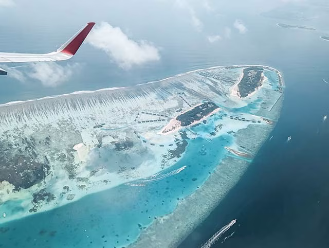 a breathtaking aerial view of the Maldives, captured from a plane. The turquoise waters of the Indian Ocean surround the islands, creating a stunning contrast with the deep blue of the sea further out. The islands themselves, with their lush greenery, appear as gems scattered across the water. This image beautifully captures the unique beauty of the Maldives, making it a perfect representation of the allure of travel.