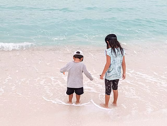 a heartwarming moment of two young siblings during their family travels in the Maldives. The children are seen playing on the sandy beach, with the turquoise waters of the Indian Ocean as their backdrop. The sky is clear, and the sunlight illuminates the scene, creating a vibrant and joyful atmosphere. This image beautifully encapsulates the essence of family travel and the unforgettable memories created during such adventures.