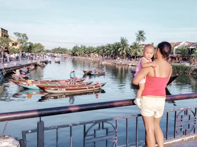 mother holding baby looking out the river with Vietnamese boats in Hoi An, Vietnam
