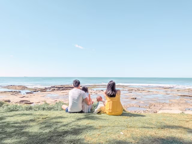 family with two young kids sitting at the beach looking out to the reef and ocean ahead