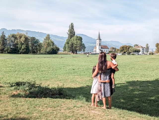 family mother holding son and daughter looking out to a church across the park in Lake Zurich, Switzerland