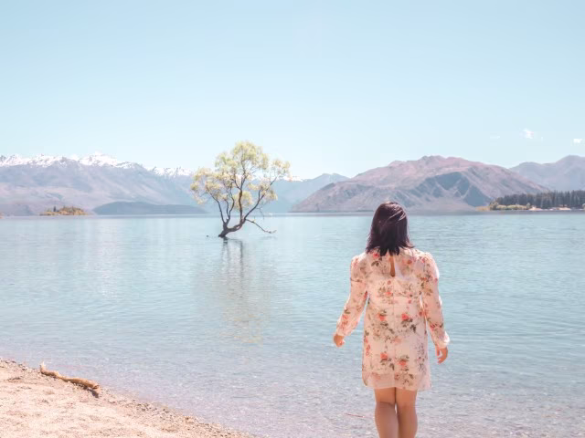 woman standing in the crystal clear water of lake wanaka with Wanaka Tree, New Zealand and alps in the distance