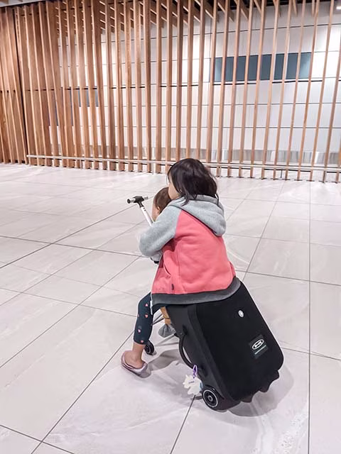 brother and sister sitting on a ride on luggage in airport