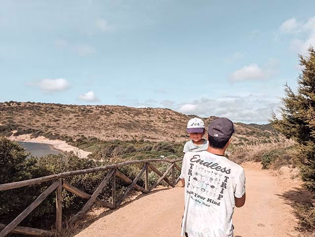 a delightful moment of a family travelling around the world with their kids. The family, consisting of two adults and a toddler, are seen from behind, walking down a path surrounded by lush greenery. The family's sense of adventure and their off-the-beaten-track approach to travel are evident in this image, making it a perfect representation of their family travel adventures.