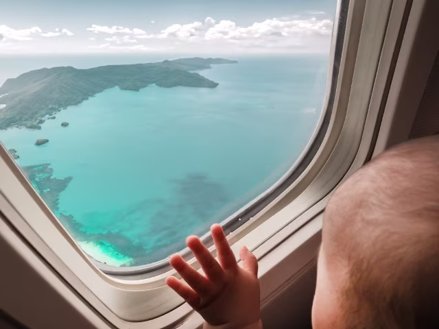 Baby looking out the plane window, turquoise water ocean island view