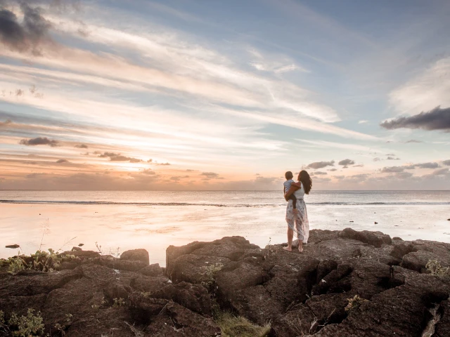woman holding baby standing on black rock rarotonga cook islands sunset ocean island breeze destination guide cover